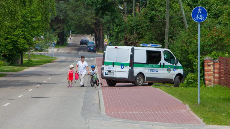 Gājēja ar bērniem apiet Reģionālās pašvaldības policijas auto, kas aizšķērsojis gājēju ietvi.